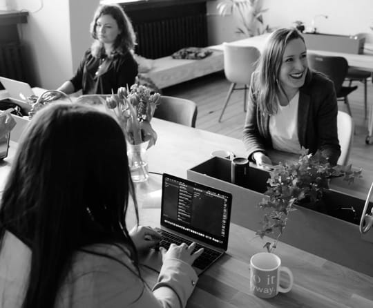 Group of professional women working on laptops at a large table in an office space